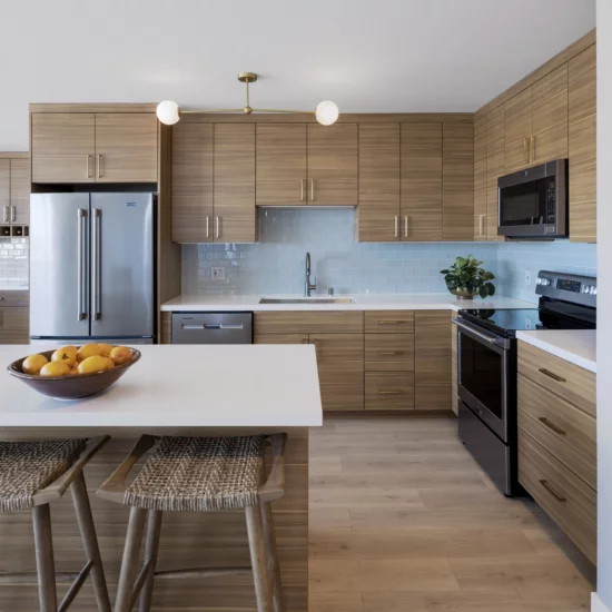 Pet Friendly Apartments in Oakland CA - 1200 Lakeshore - A Modern Kitchen With Hardwood Flooring, Light Wood Cabinets, White Counters, Stainless Steel Appliances, And A Kitchen Island With Bar Seating